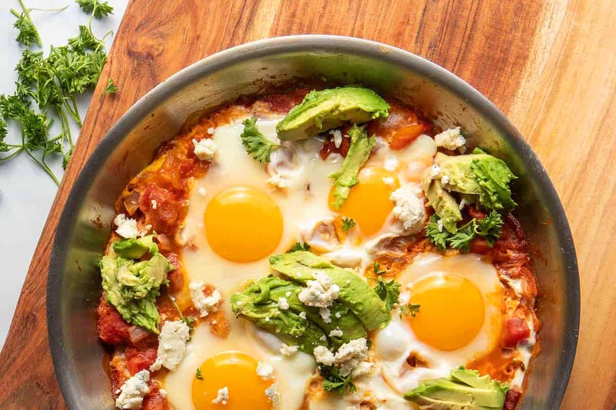 A skillet filled with eggs and avocado on a wooden cutting board.
