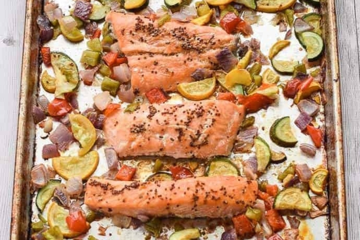 Salmon and vegetables on a baking sheet, drizzled with apple cider.