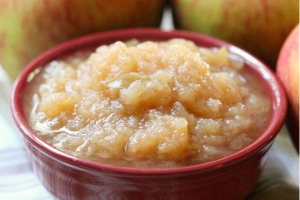 Applesauce in a bowl with apples next to it.
