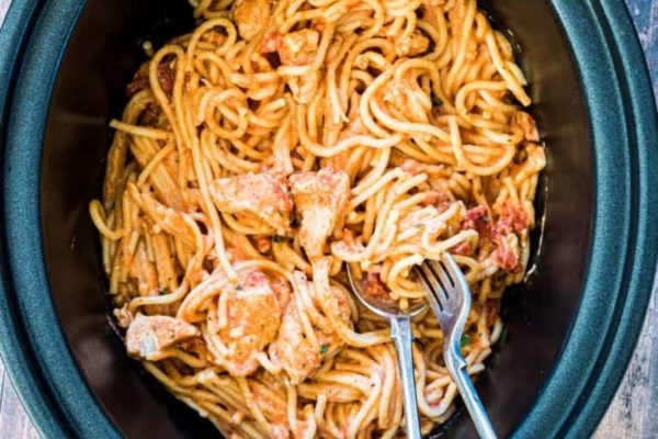 A crock pot filled with spaghetti and chicken.