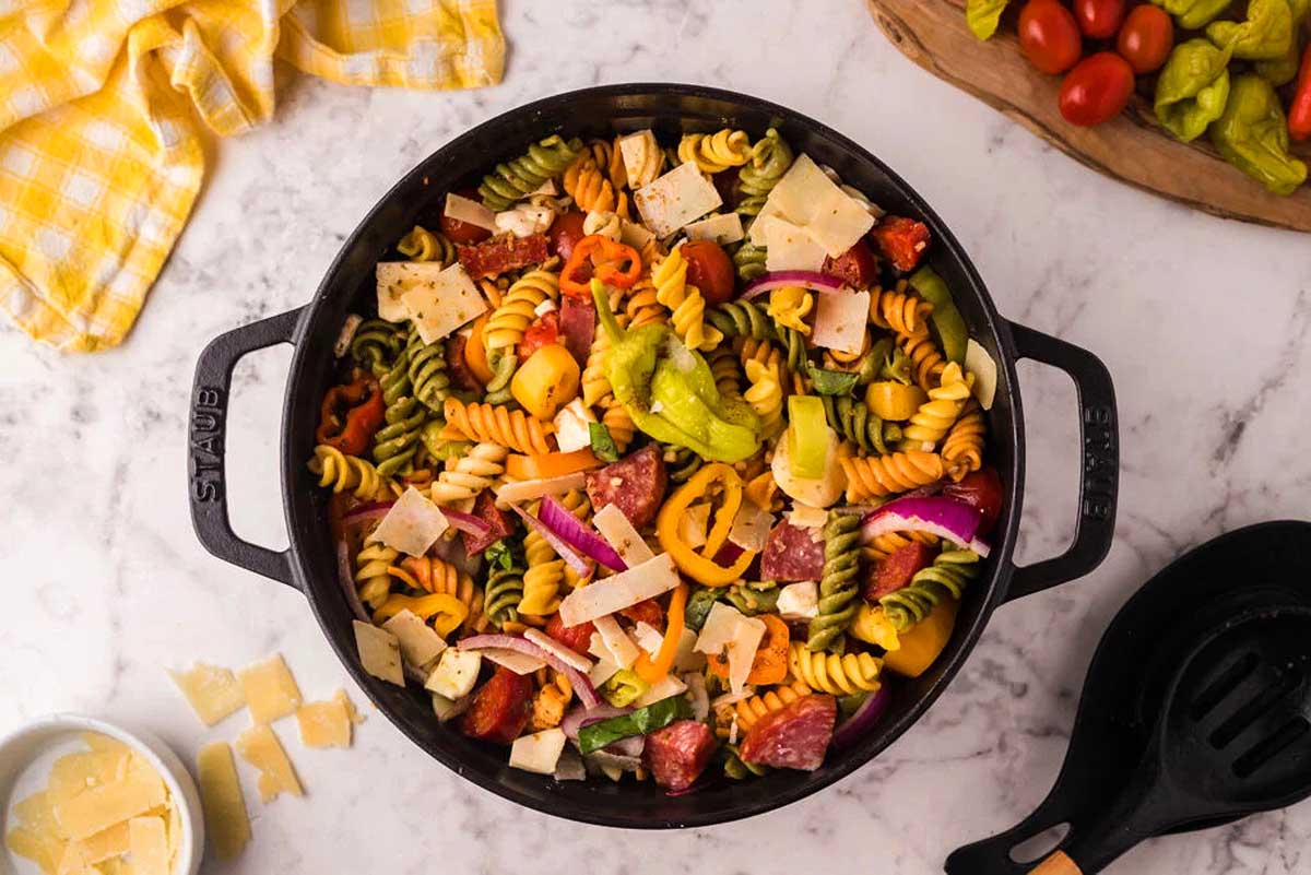 A pan full of pasta and vegetables on a marble countertop.