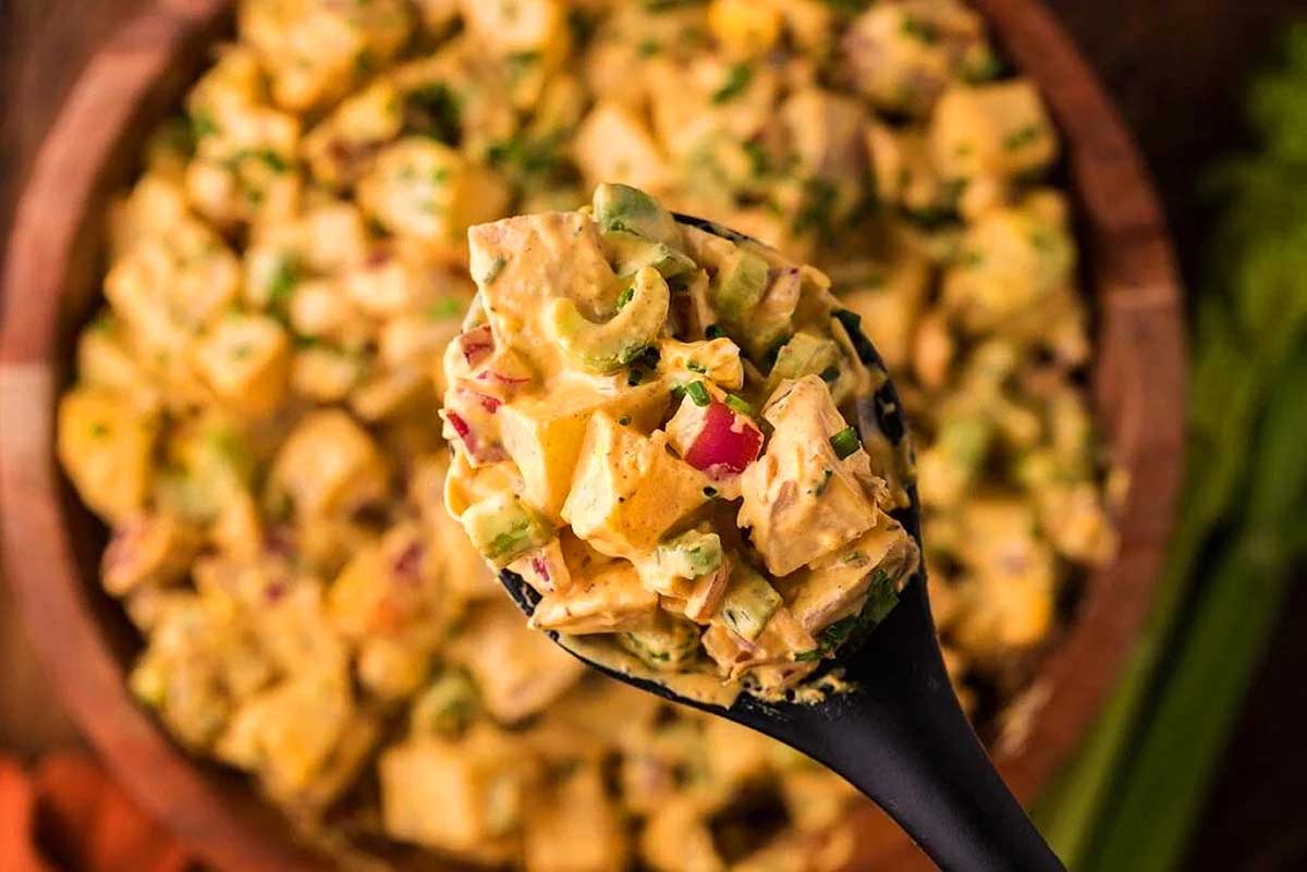 A spoon full of potato salad on a wooden table. This is one of the best potato salad recipes.