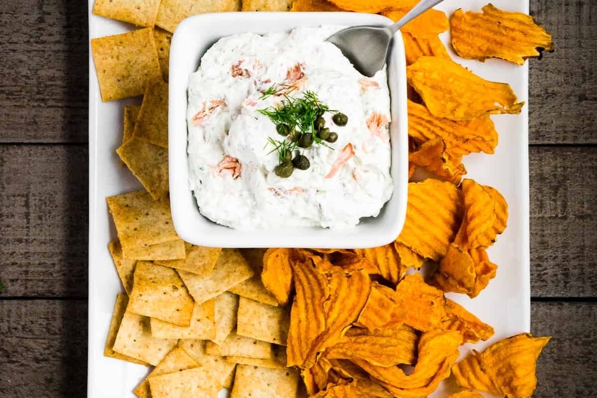 Christmas party appetizers featuring smoked salmon dip served on a white plate, accompanied by crackers.