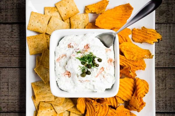 A white bowl with dip and crackers on it.