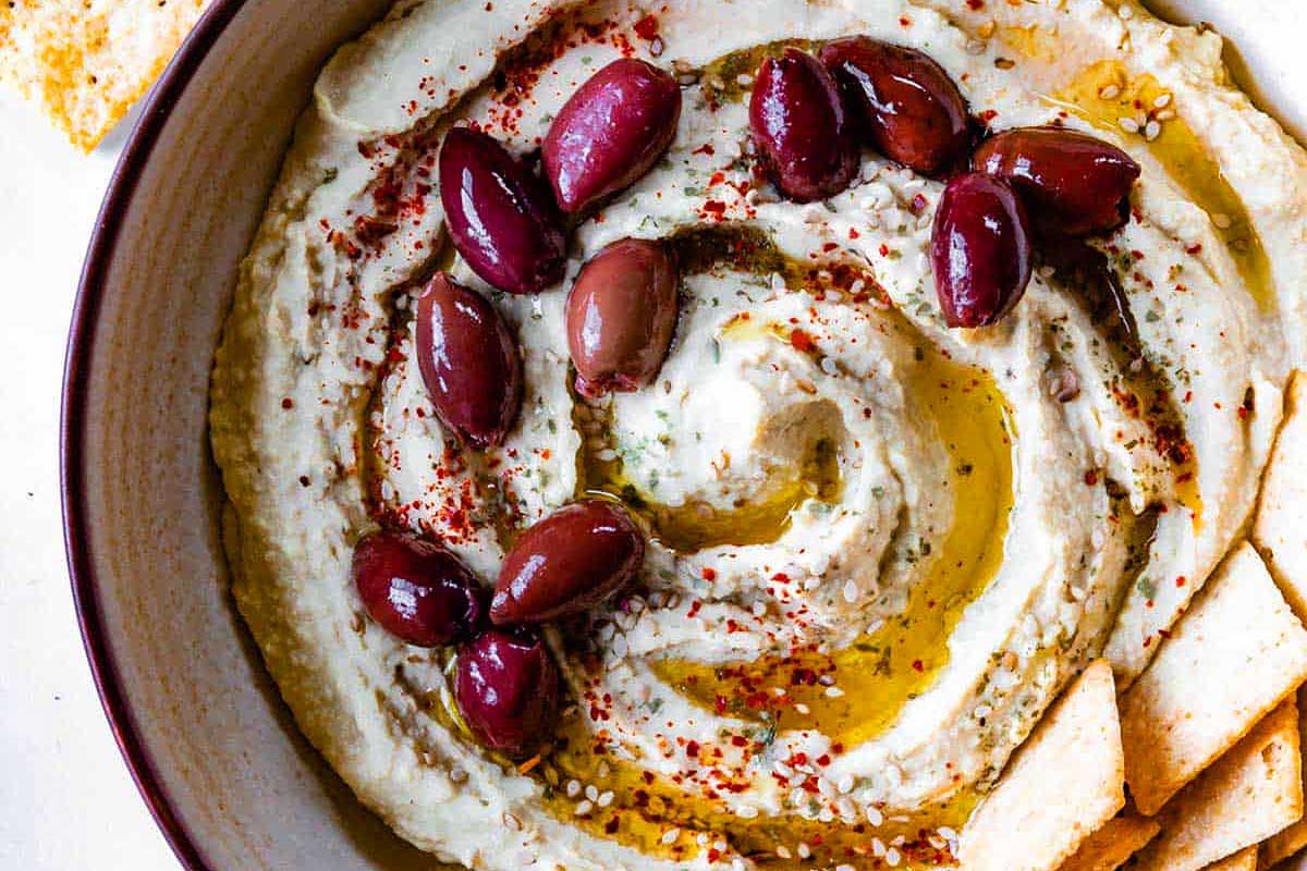 Hummus with olives and crackers in a bowl.
