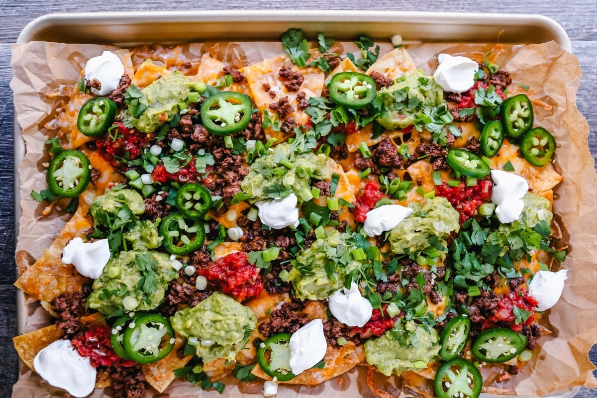 Nachos on a baking sheet with guacamole and sour cream.