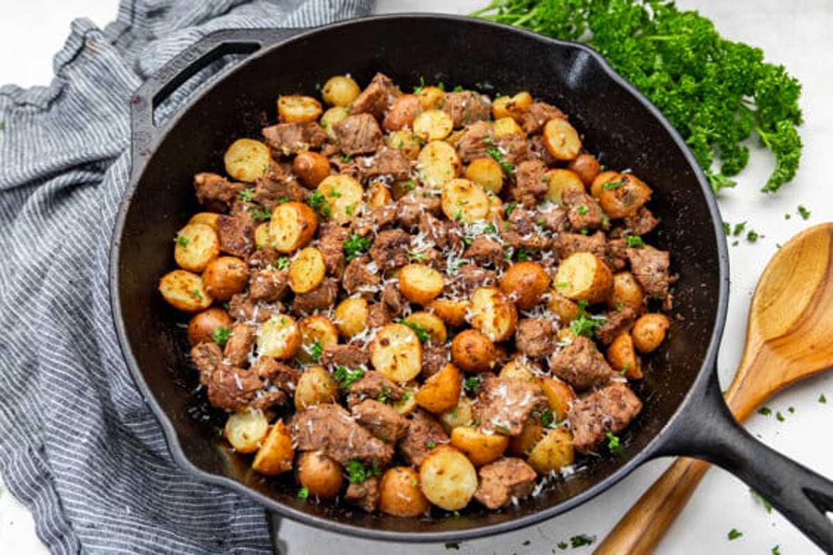 A skillet with meat, potatoes and parsley.