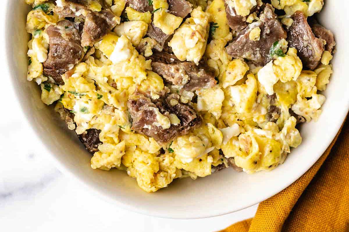 A bowl of scrambled eggs with meat and herbs.