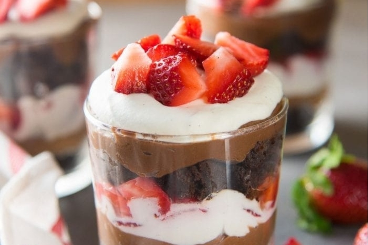 A chocolate strawberry trifle in a glass with whipped cream and strawberries. This dessert delight combines layers of decadent chocolate, succulent strawberries, and fluffy whipped cream to create a heavenly treat that