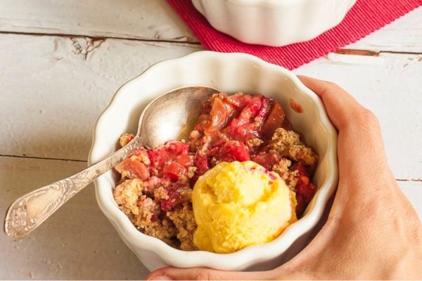 A hand holding a bowl of cranberry crumble with ice cream.