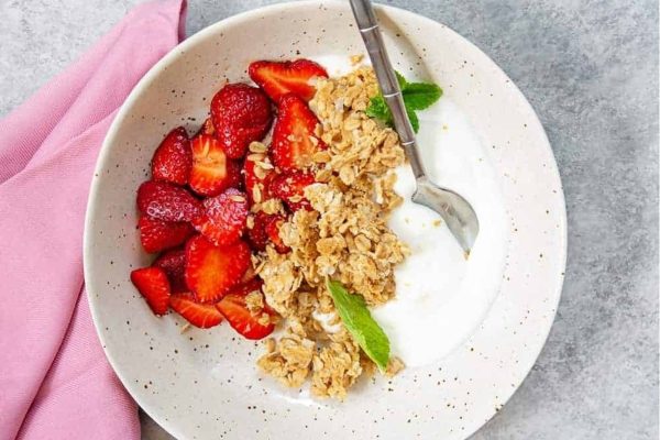 Granola, yogurt and strawberries in a white bowl topped with coconut shavings.
