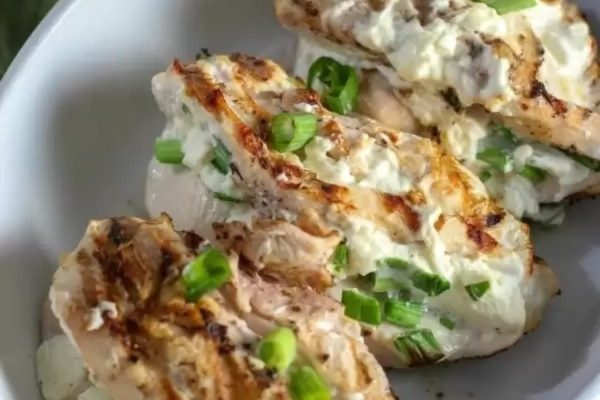 Grilled chicken breasts on a white plate with green onions.