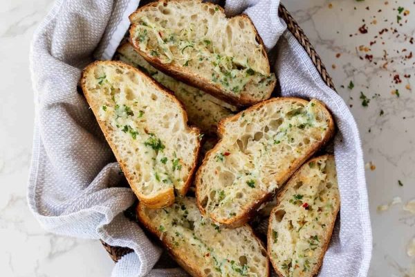 Sliced garlic bread in a basket on a marble table.