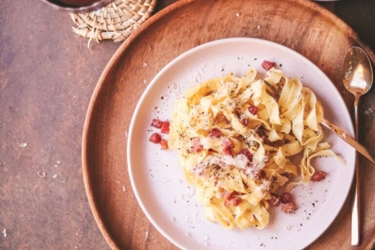 A plate of Italian pasta with ham and parmesan on a wooden table.