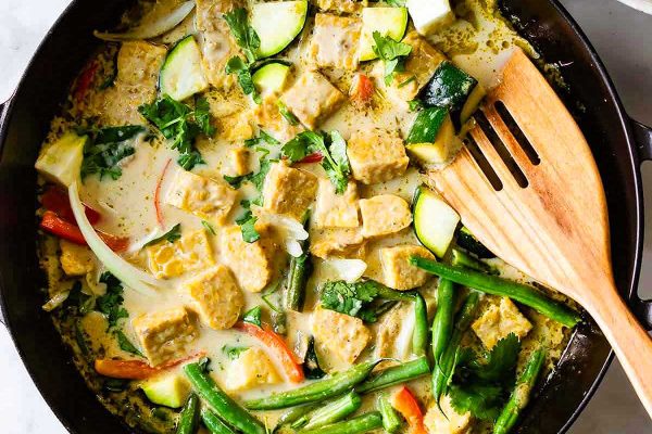 Thai tofu stir fry in a skillet with vegetables and a wooden spoon.