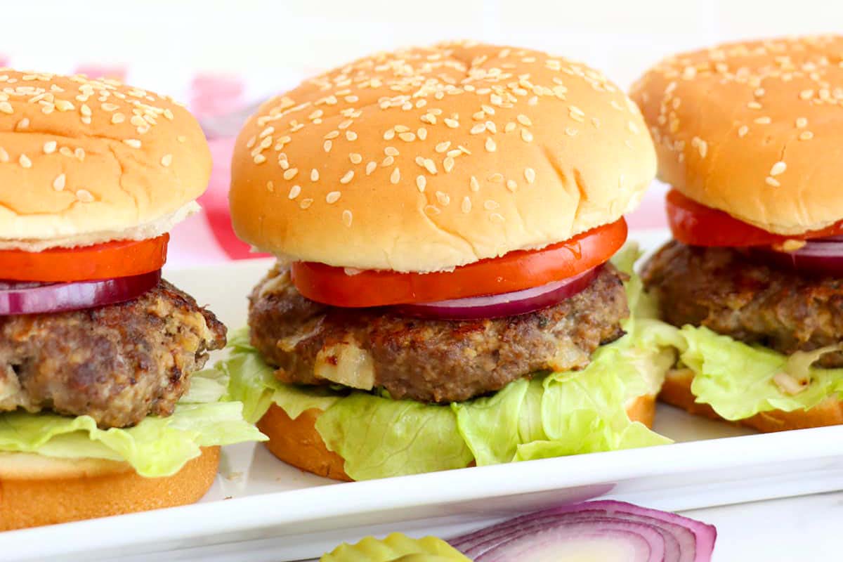 Four hamburgers are sitting on a white plate.
