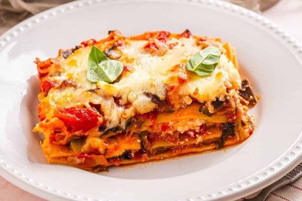 A plate of lasagna with vegetables and herbs.