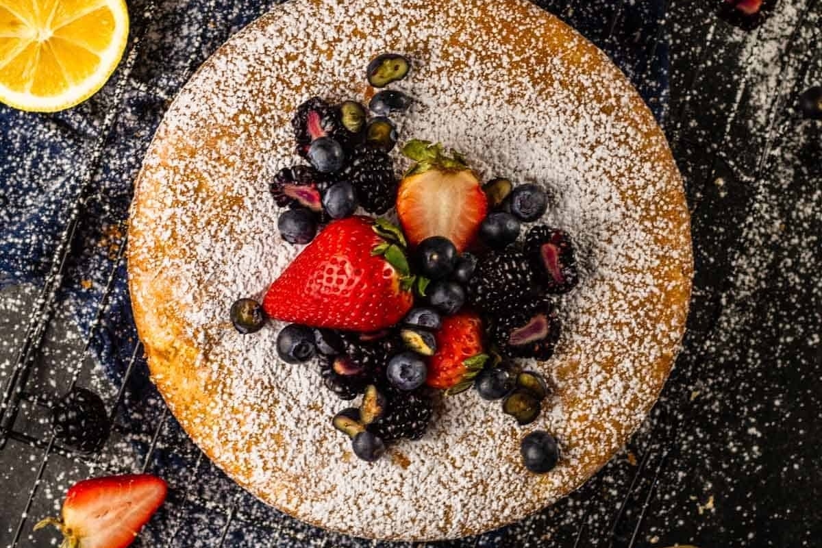 A refreshing Italian dessert featuring a cake infused with tangy lemon flavor, topped with luscious berries and delicately dusted with powdered sugar.