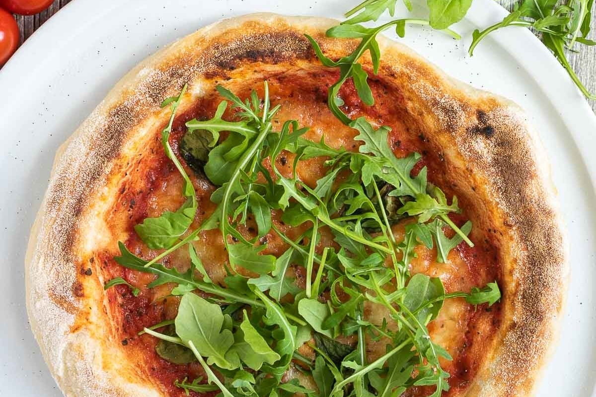An Italian pizza with arugula and tomatoes on a white plate.