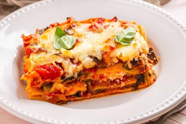 A plate of lasagna with tomatoes and basil on it.