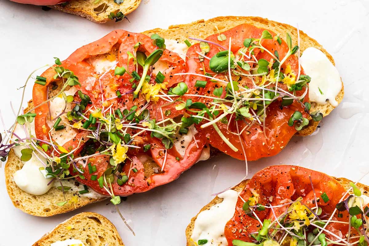 A delicious tomato sandwich recipe with sprouts on a slice of bread.