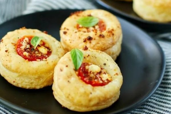 A plate topped with mini pizzas with tomatoes and basil.