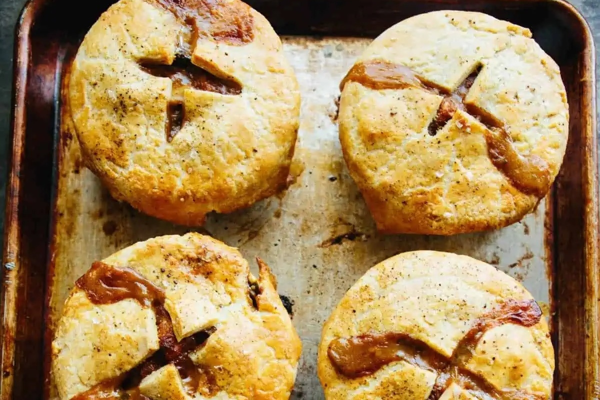 Four savoury meat pies on a baking sheet.