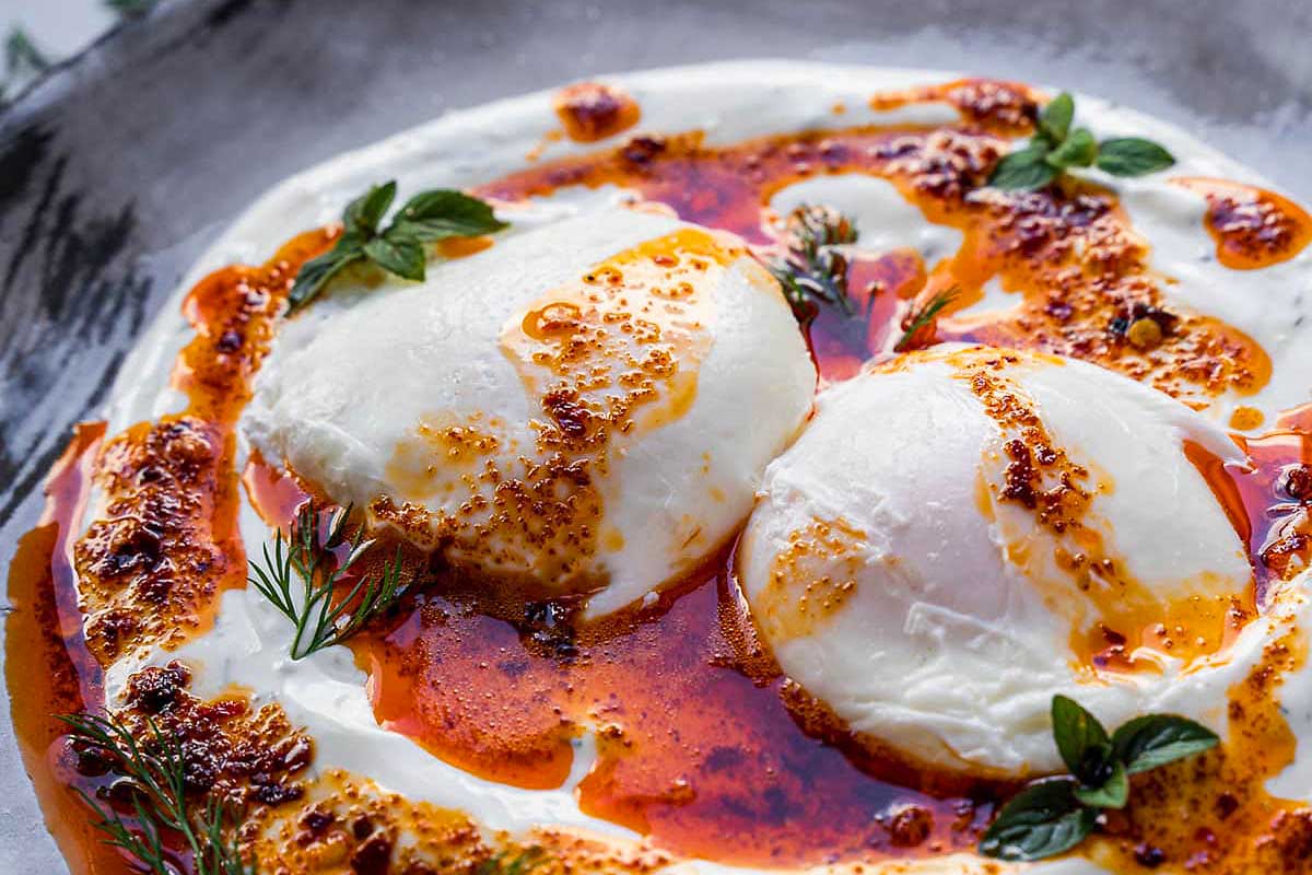 Two eggs on a plate with sauce and herbs.