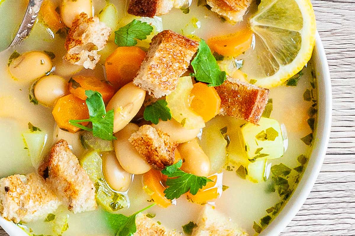 A bowl of white bean soup with croutons and lemon wedges.