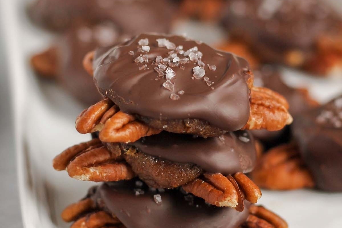 A stack of chocolate covered pecans, a holiday treat, on a white plate.