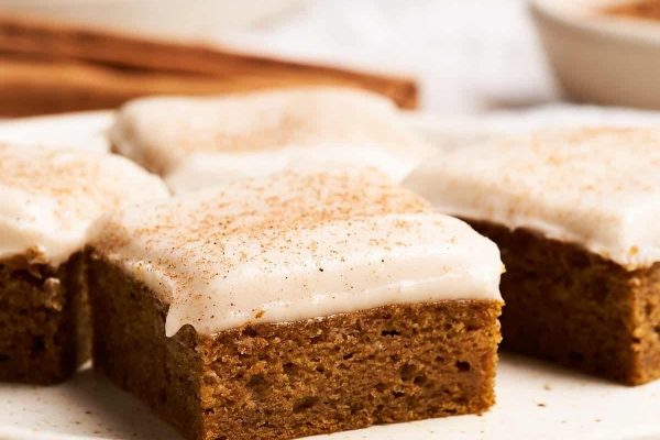Four squares of pumpkin cake with icing on a plate.