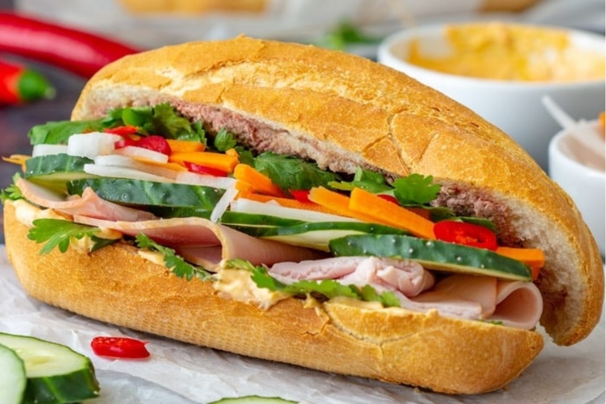 A vietnamese sandwich with vegetables and cucumbers, served on a bun.