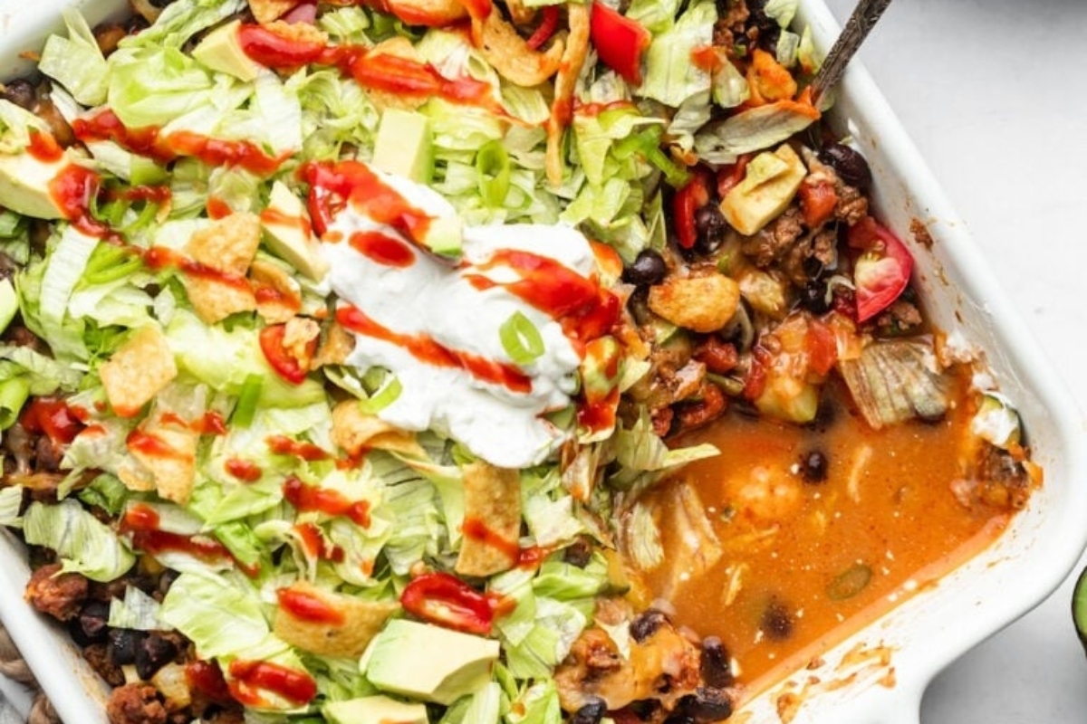 Mexican casserole in a white dish with sour cream and avocado.