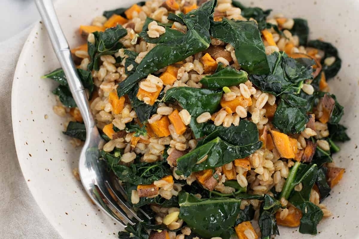 A bowl of farro and sweet potato salad with a fork.