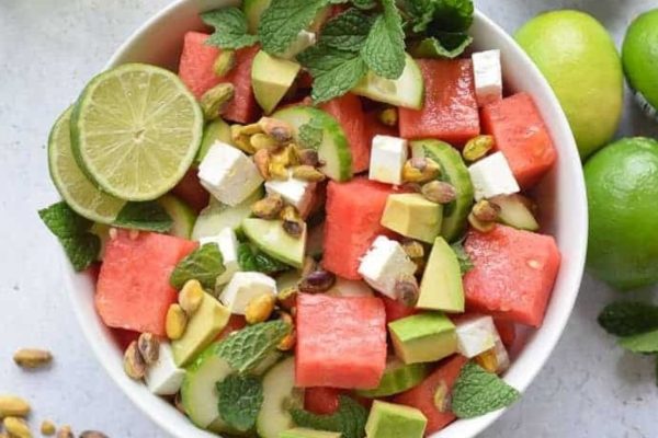 Colorful watermelon salad in a white bowl with limes.