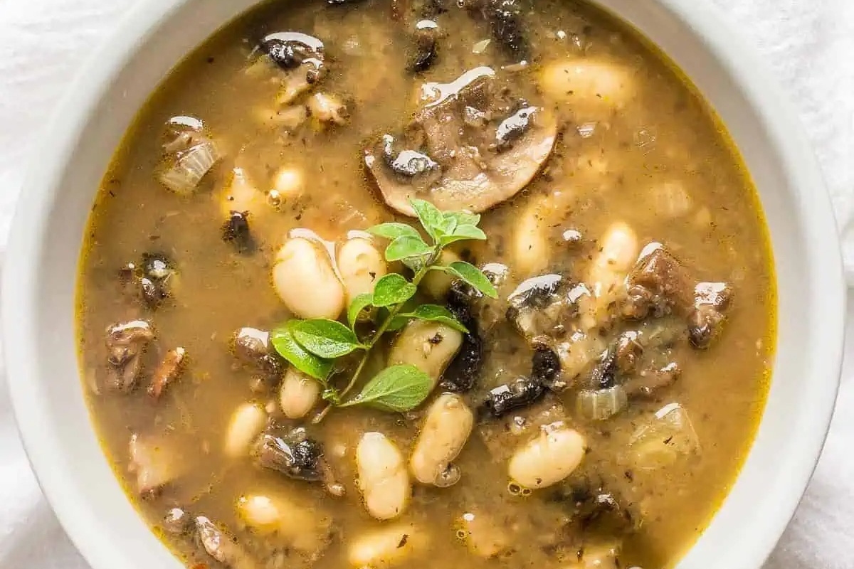 White bean and mushroom soup in a white bowl. This mushroom recipe is perfect for a cozy meal.