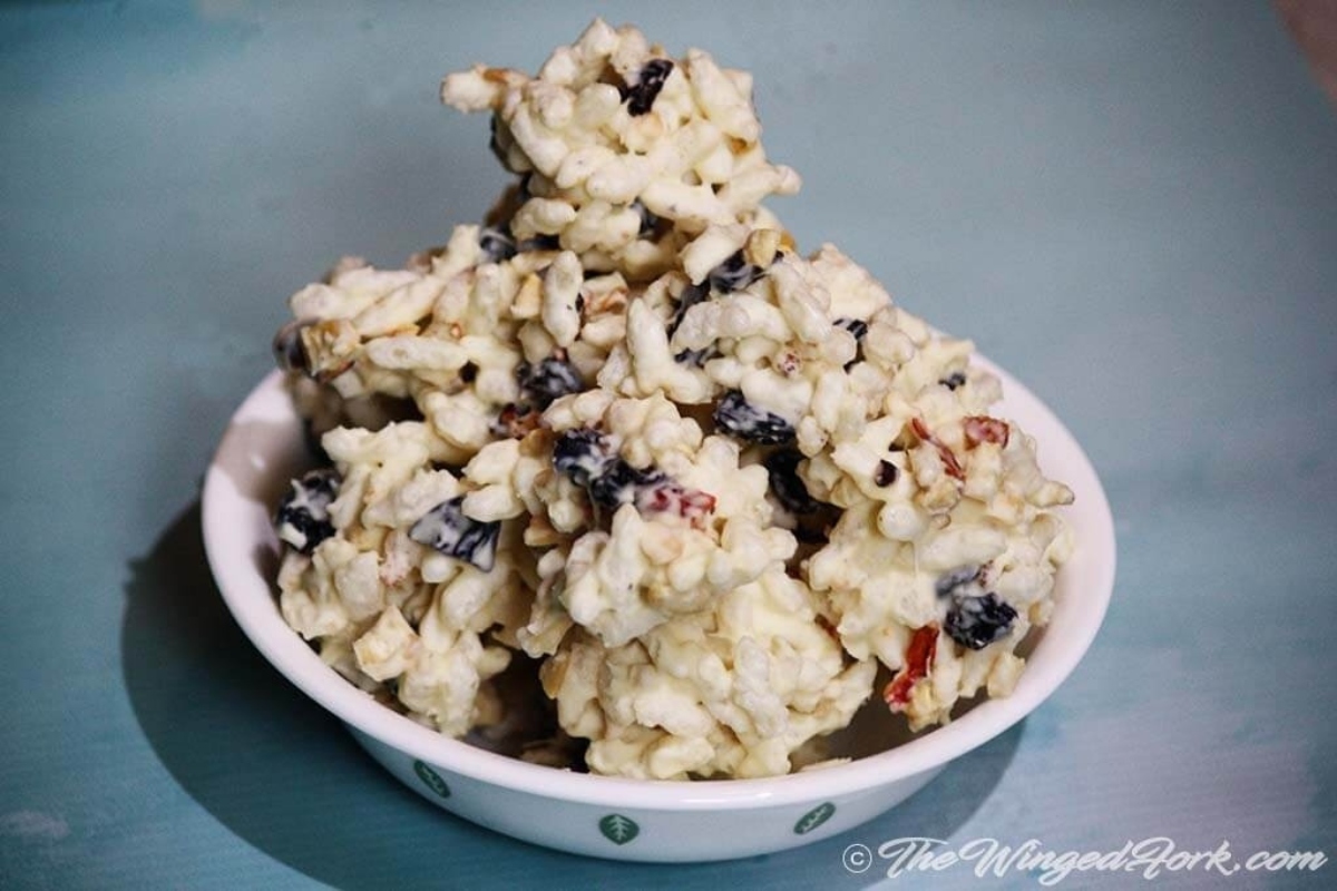 A white bowl filled with blueberry rice krispies drizzled with white chocolate.
