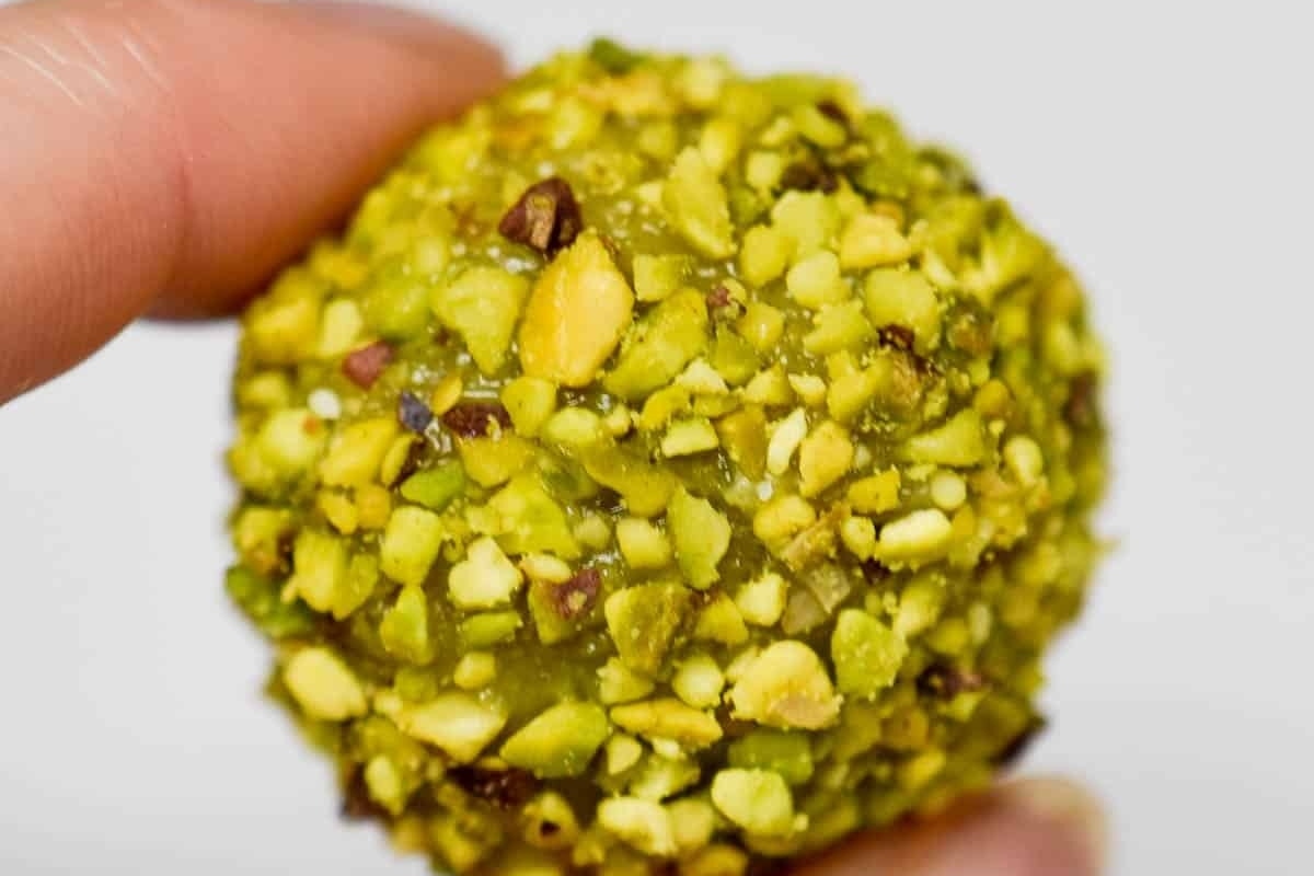 A person holding a No Bake pistachio ball with nuts on it, perfect for the holidays or as a festive dessert.