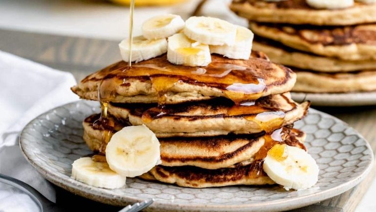 A stack of pancakes with syrup and bananas on a plate.