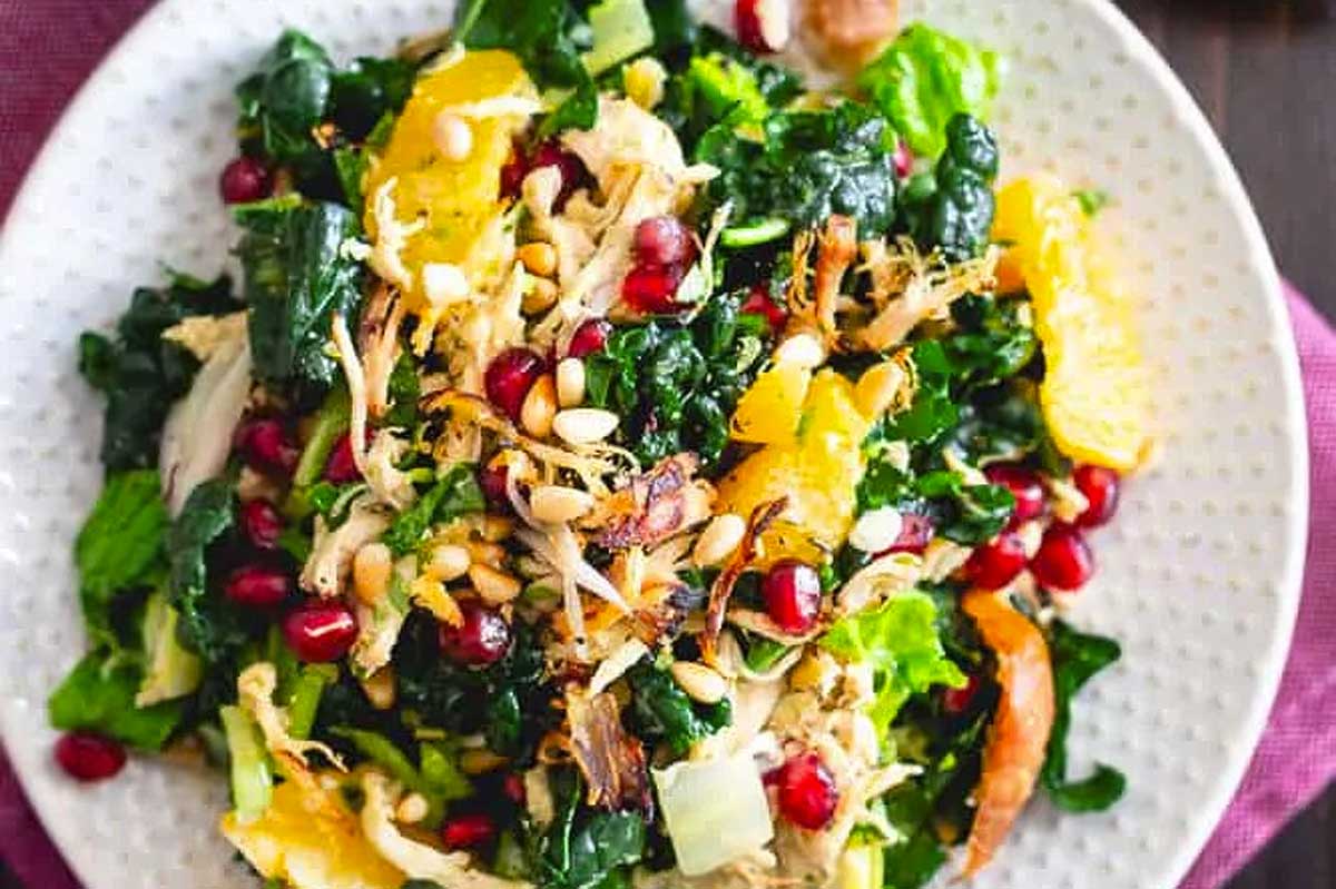 A plate of kale salad with chicken and pomegranate.