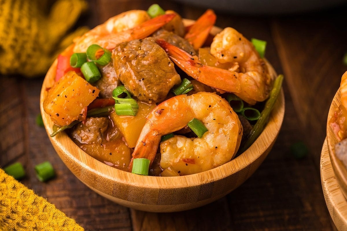 An Asian-inspired bowl of shrimp and beef stew on a wooden table.