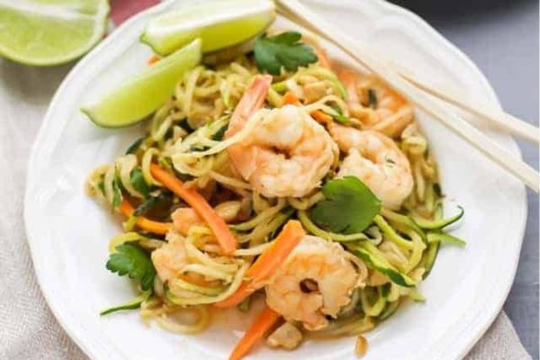 Thai shrimp noodles on a white plate with chopsticks, perfect for a feast with friends.