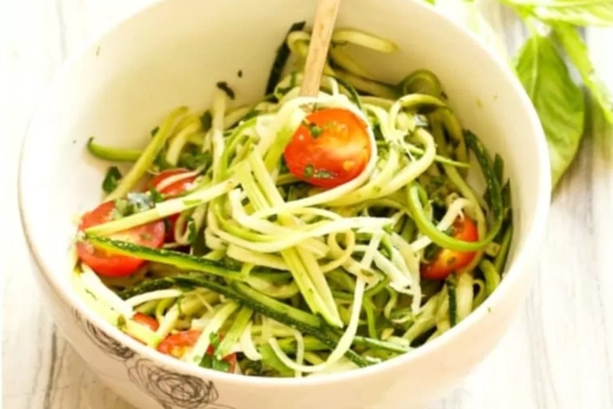 Zucchini noodles tossed in a flavorful pesto sauce, garnished with fresh tomatoes and basil leaves.