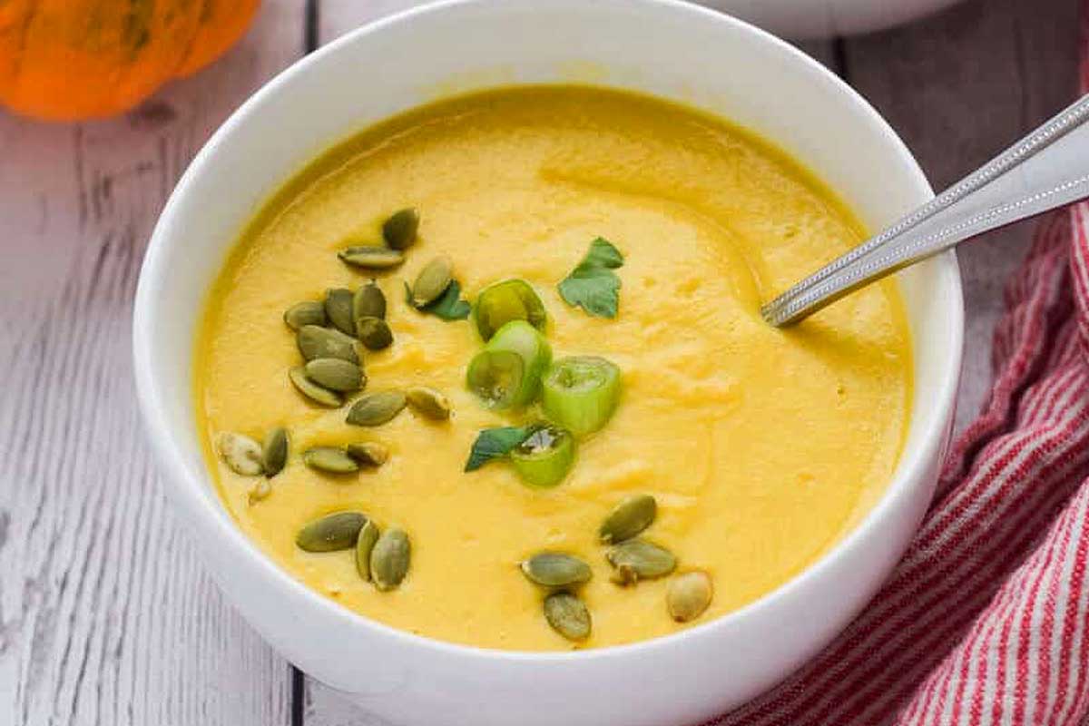 Vegan pumpkin soup in a white bowl with pumpkin seeds, perfect for Thanksgiving.