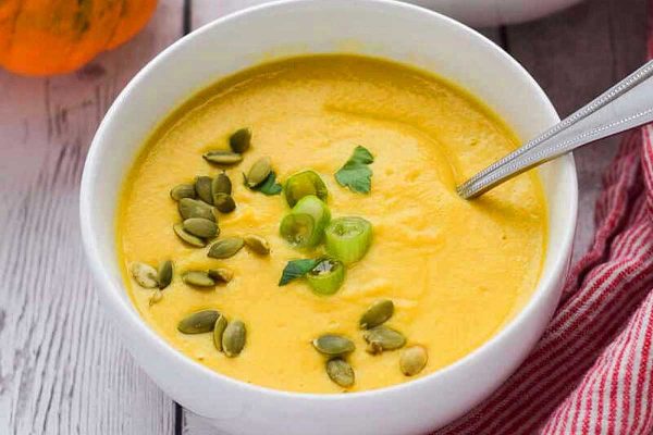 Pumpkin soup in a white bowl with pumpkin seeds.