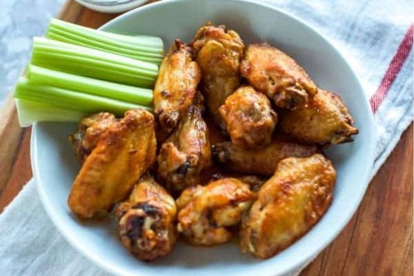 Chicken wings in a bowl with celery and dipping sauce.