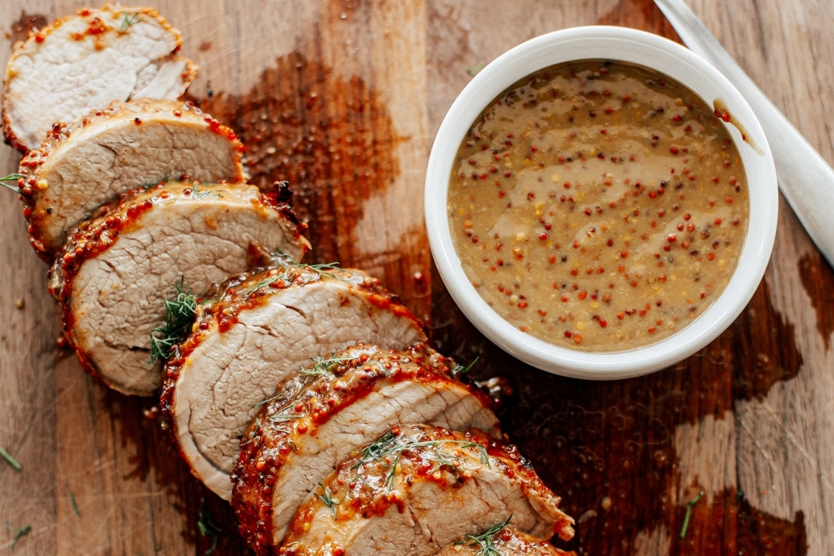 Winter recipe for sliced pork tenderloin with a dipping sauce, prepared in an air fryer and served on a wooden cutting board.