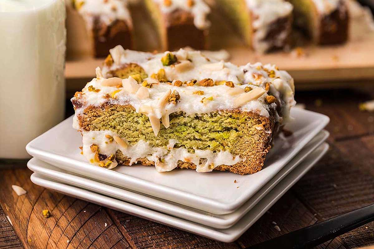 A delectable slice of pistachio bread expertly presented on a plate, accompanied by a refreshing glass of milk.