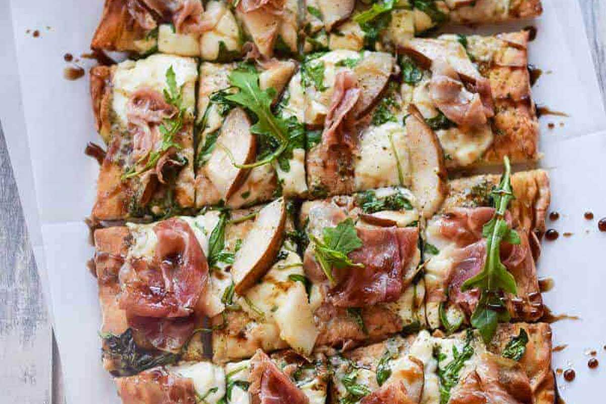 A pizza with prosciutto and arugula on a white plate.