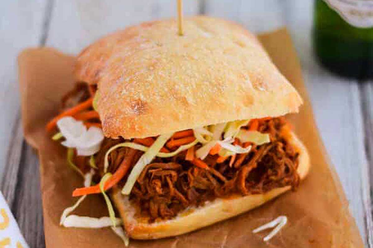 A pub staple - a pulled pork sandwich topped with coleslaw and accompanied by a refreshing beer.
